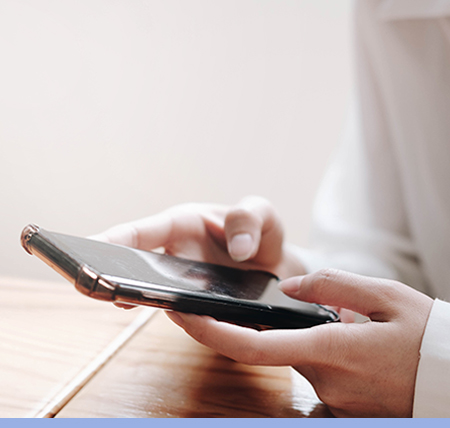 Eine Frau mit einer weissen Bluse hält ein Smartphone in der Hand und tippt etwas auf ihrem Handy ein.